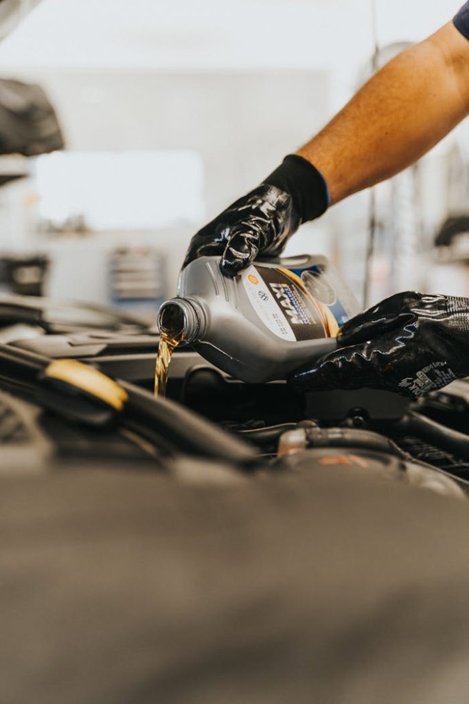 pexels-photo-13065693 Close-up of a mechanic pouring engine oil into a car engine with gloved hands, indoors.